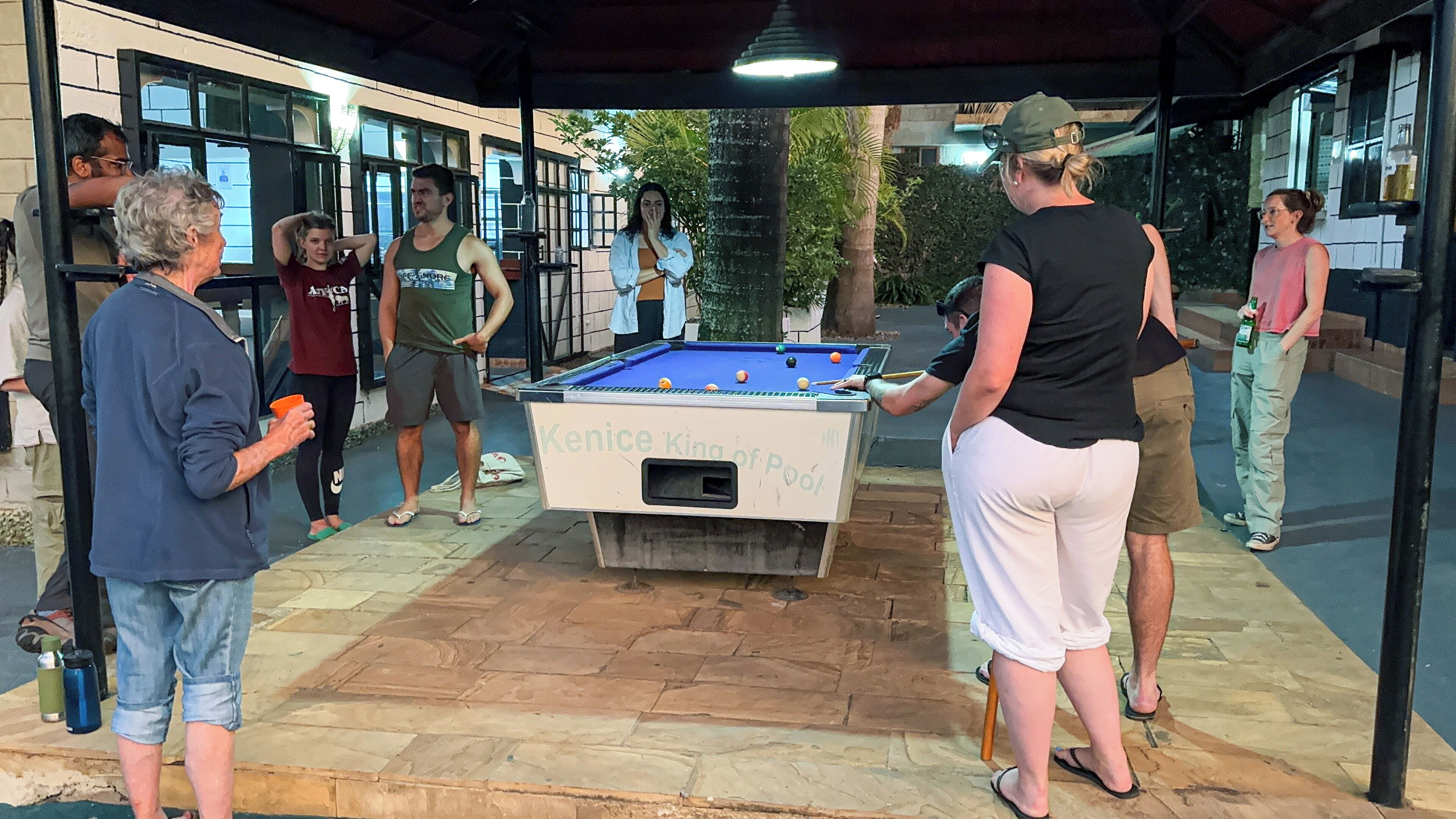 A pool table in an outdoor setting with a stone floor and a covered area.