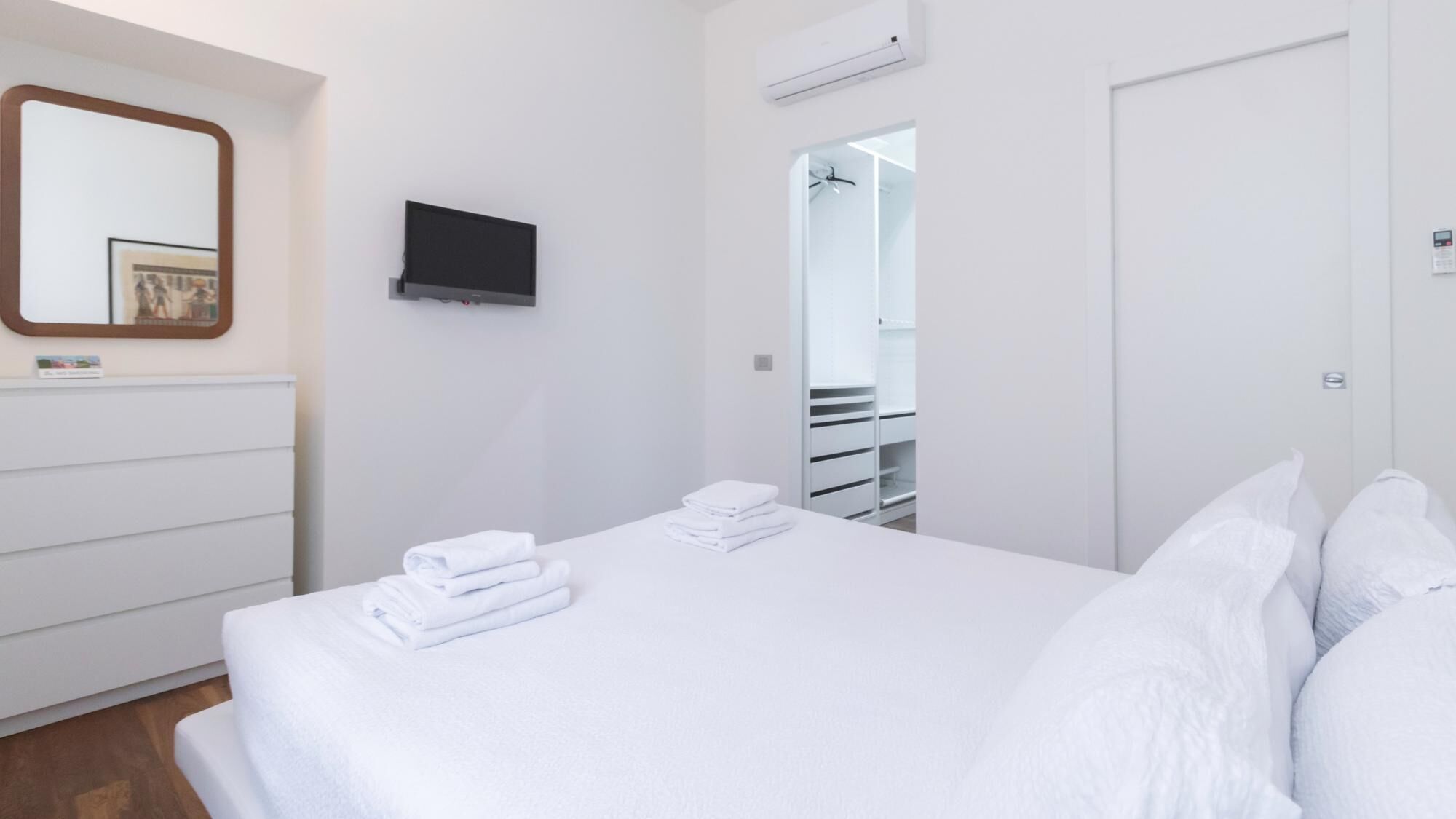 Une chambre d’hôtel avec un lit soigneusement fait, un téléviseur fixé au mur et une porte donnant accès à la salle de bain.