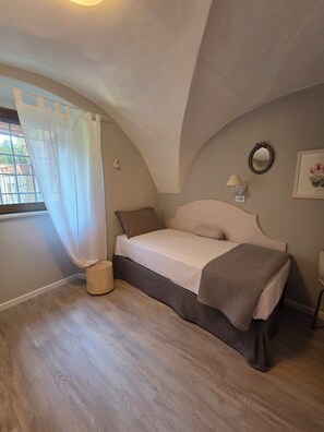 A bedroom with a bed, a bedside table, a lamp, a wall clock, and a window with a curtain. - "Volta" Apartment: Patio & Reserved Space (Trentino-Alto Adige)