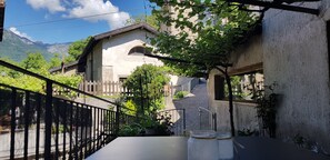 Un patio con una mesa, un edificio de fachada de piedra y montañas al fondo.