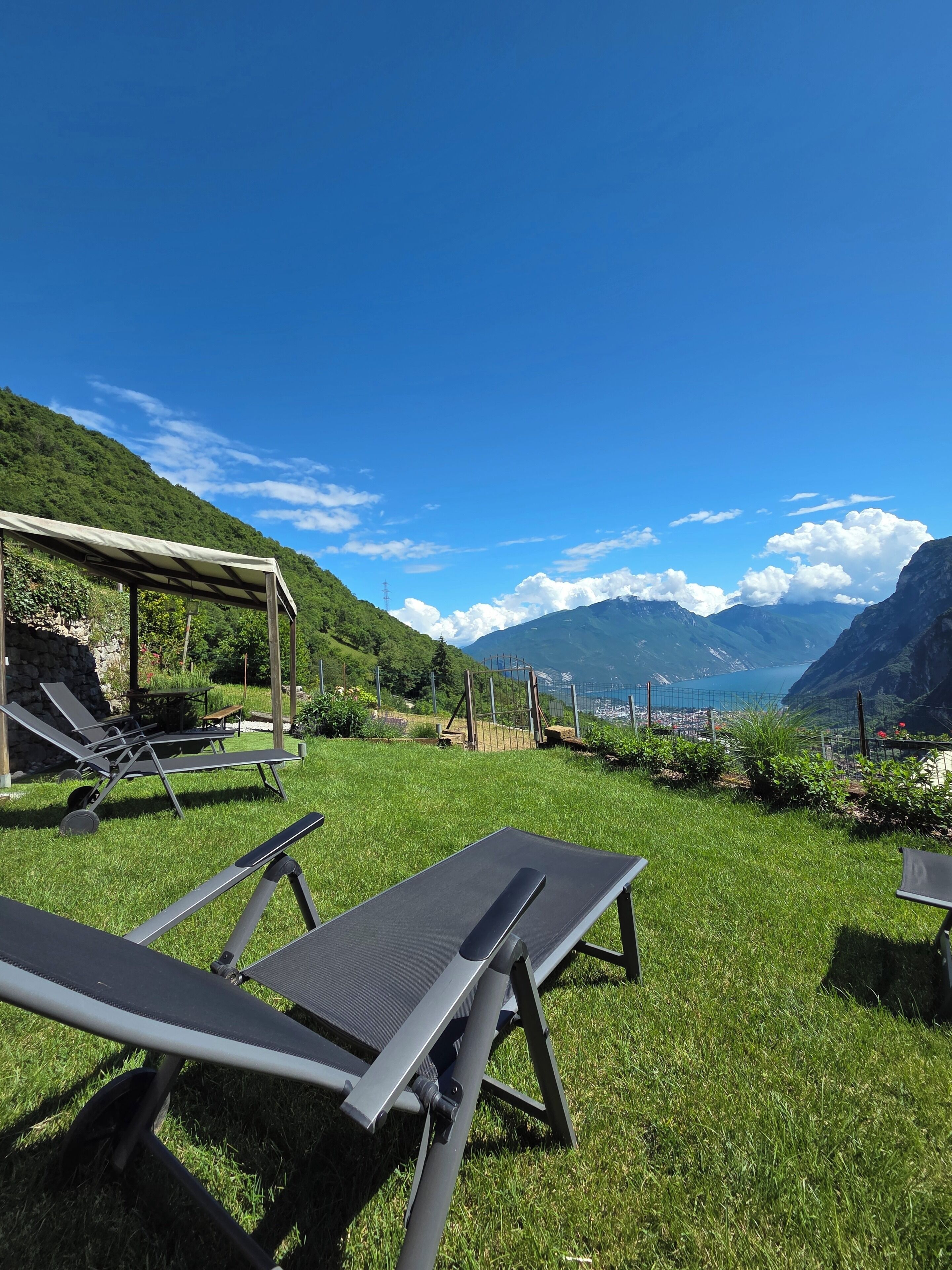 Un espace extérieur verdoyant, doté de chaises longues et d’un coin salon abrité, offrant une vue sur un paysage montagneux et une étendue d’eau.