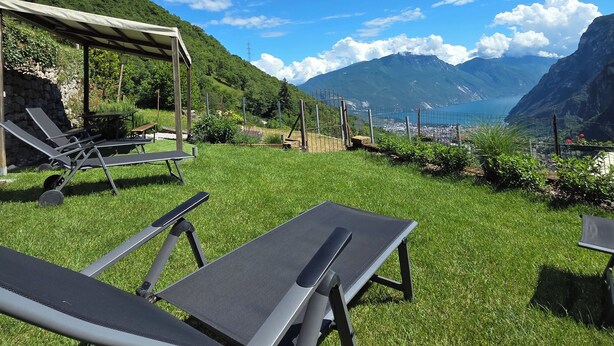 Un espace extérieur verdoyant, doté de chaises longues et d’un coin salon abrité, offrant une vue sur un paysage montagneux et une étendue d’eau.