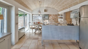 A kitchen with stone walls, a central island, and a refrigerator. - Pigreco 6 2 (Ostuni)