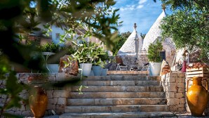 A stone staircase leading to a building with a conical roof, outdoor seating, and large vases. - Pigreco 6 2 (Ostuni)