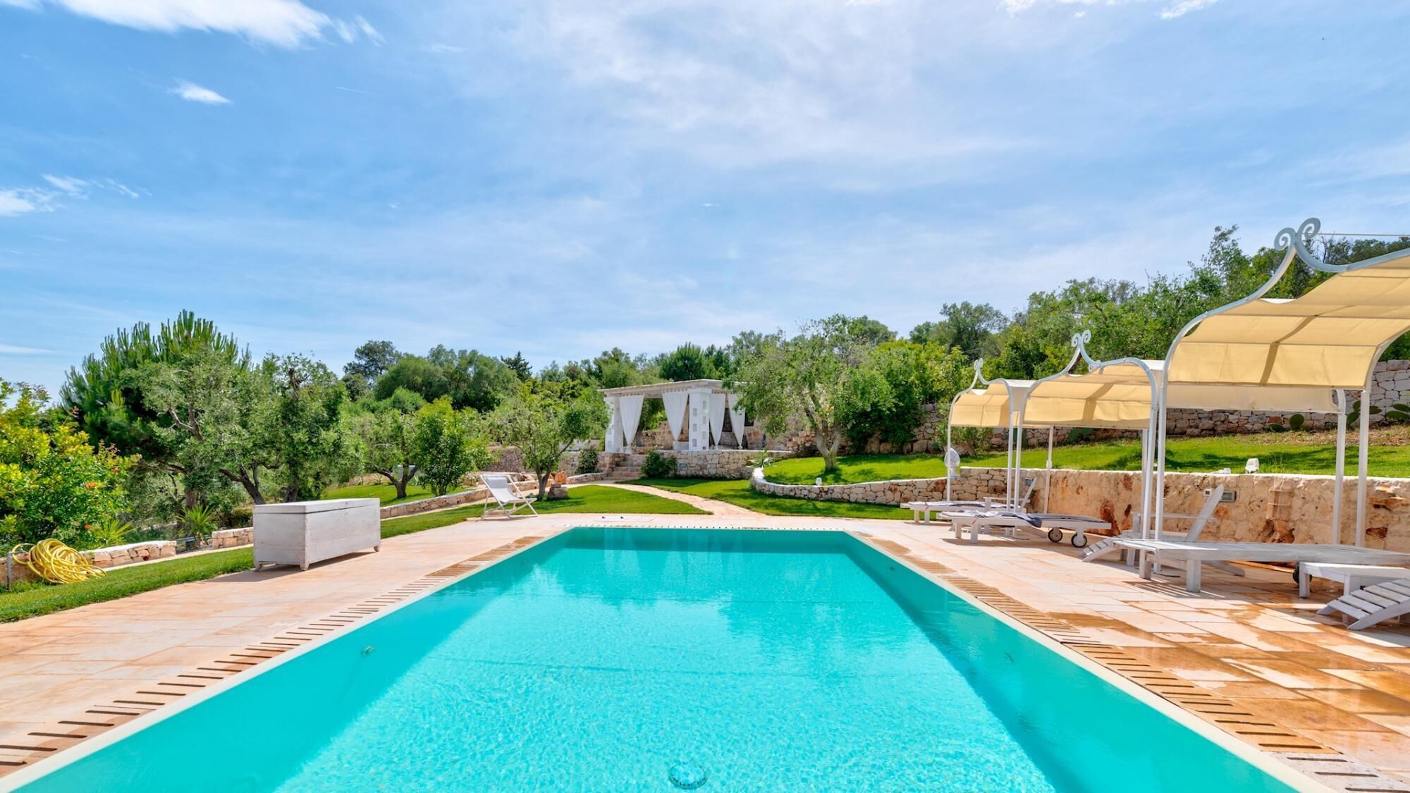 A rectangular swimming pool with a tiled deck, surrounded by lounge chairs and umbrellas.
