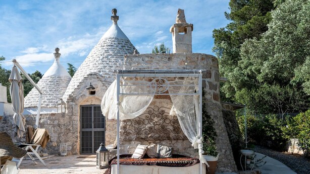 A stone house with conical roofs, a bed with a canopy, and a small balcony. - Pigreco 6 2 (Ostuni)
