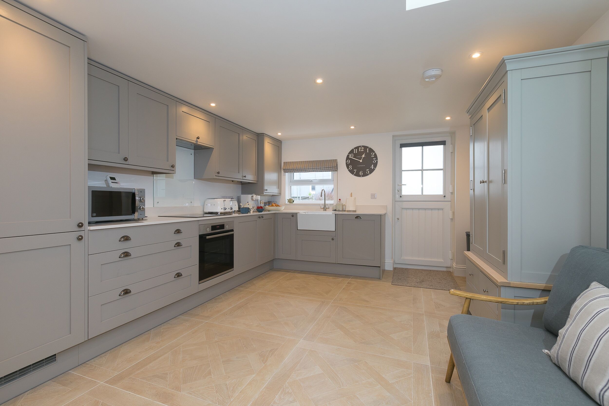 A modern kitchen with grey cabinets, a microwave, a toaster, and a sink. There is a clock on the wall and a window with a view.