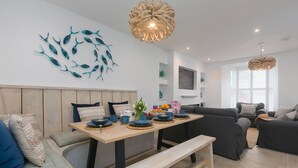 A modern living room with a wooden dining table, black sofas, and a wall-mounted fish art piece. - Pebbles (St Ives)