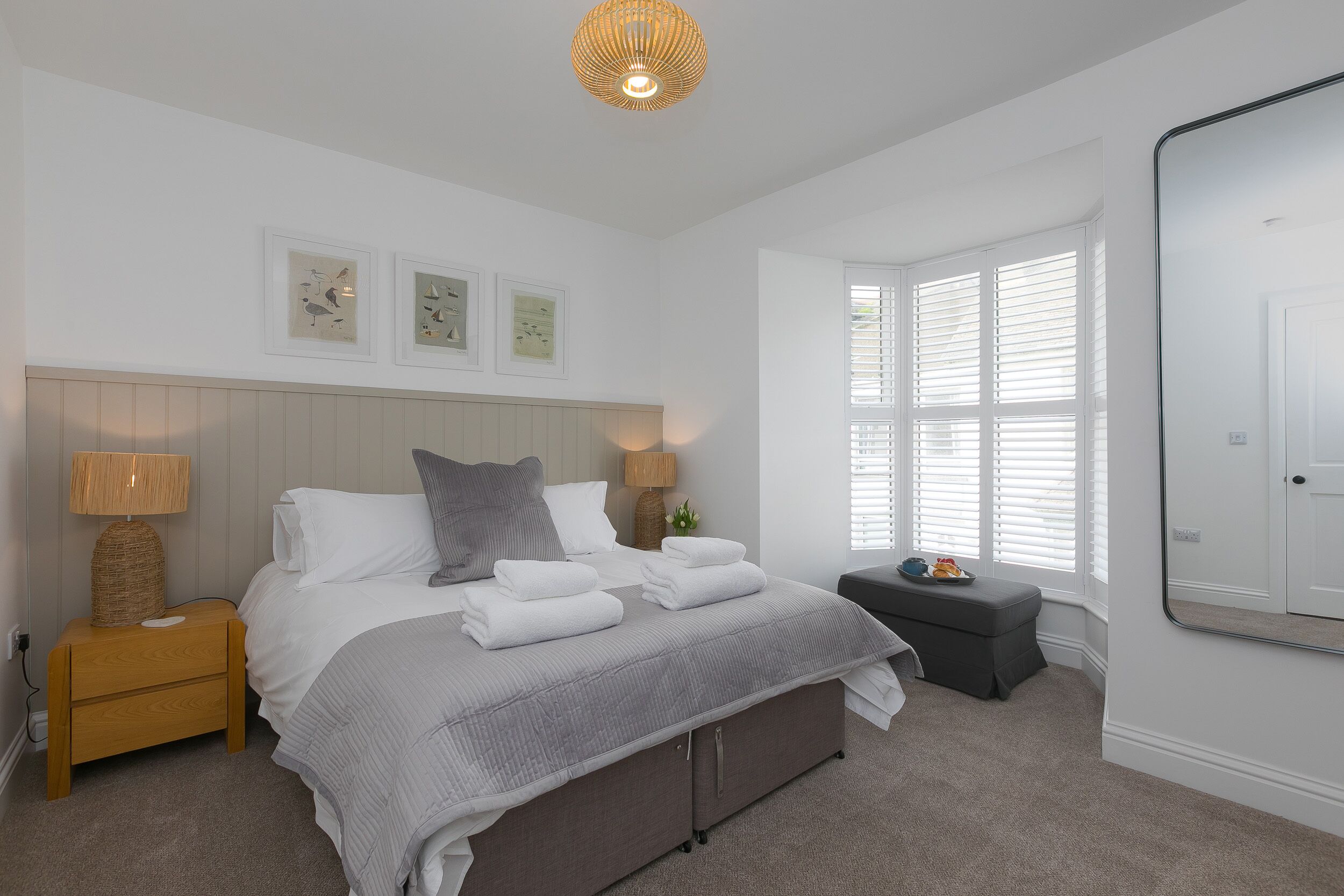 A bedroom with a bed, bedside tables, a window with blinds, a mirror, and wall art.