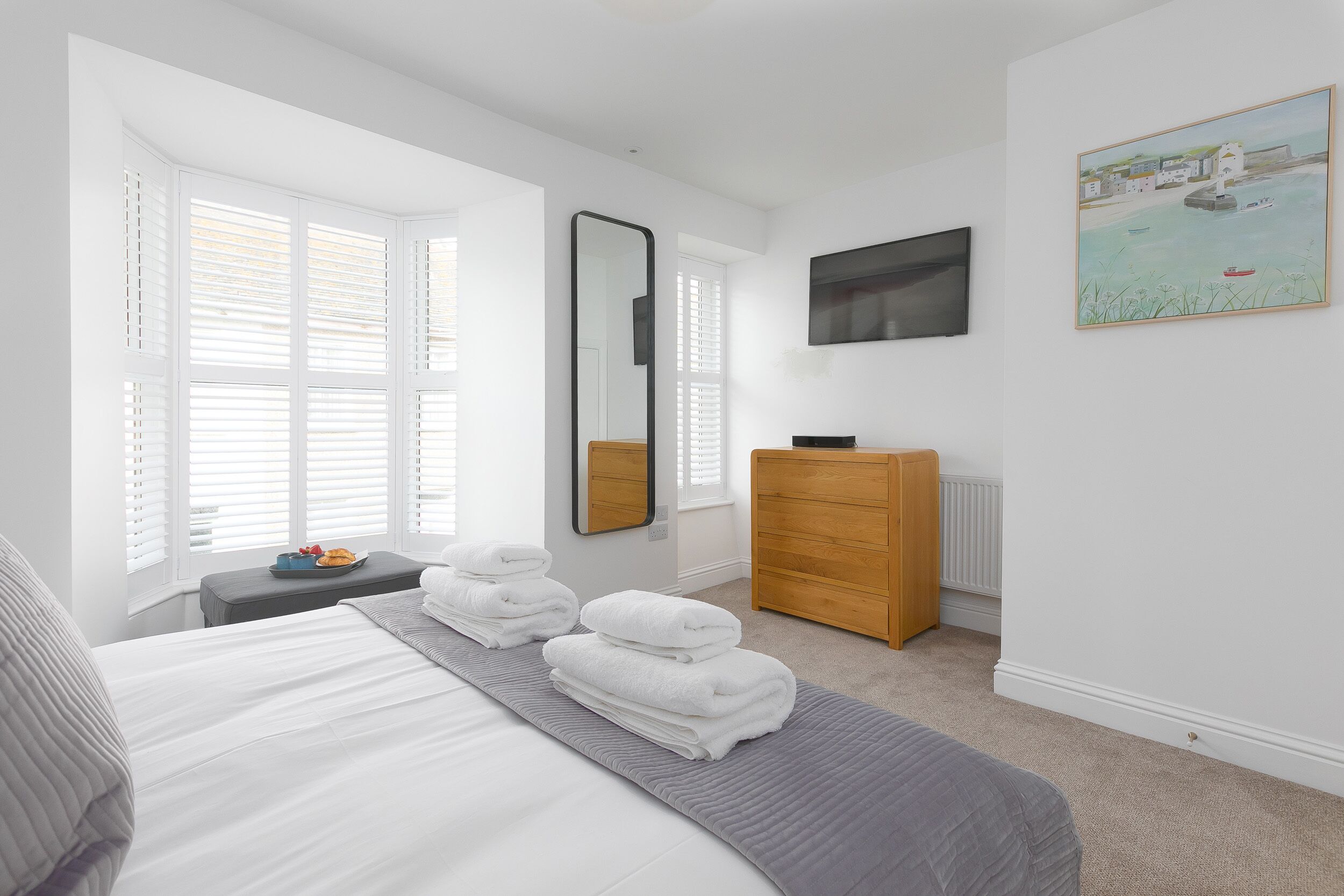A bedroom with a bed, a dresser, a mirror, and a painting on the wall.