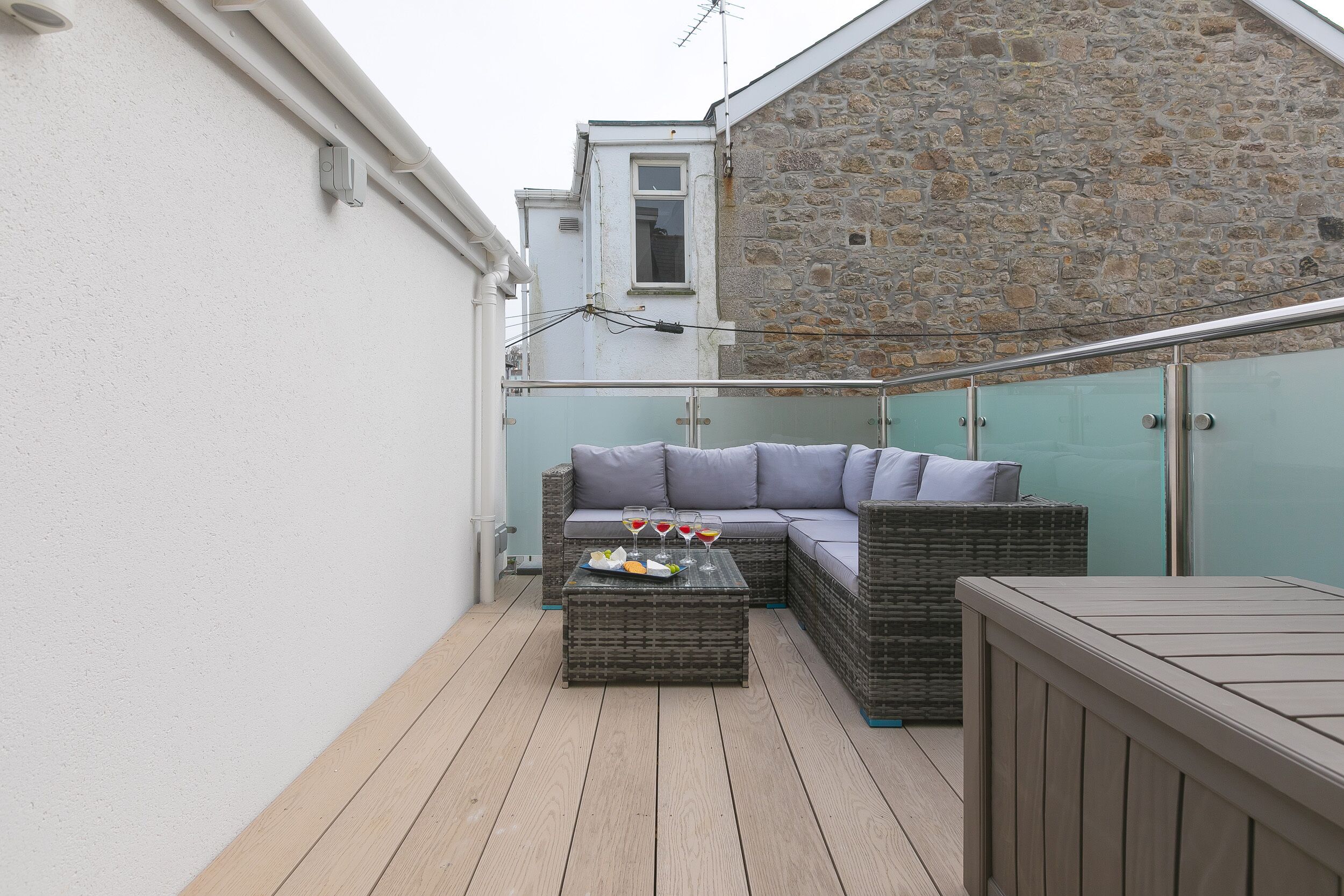 Un balcon agrémenté de meubles en osier, d’une table en bois et d’un mur en pierre.