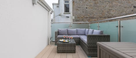 A balcony with wicker furniture, a wooden table, and a stone wall.