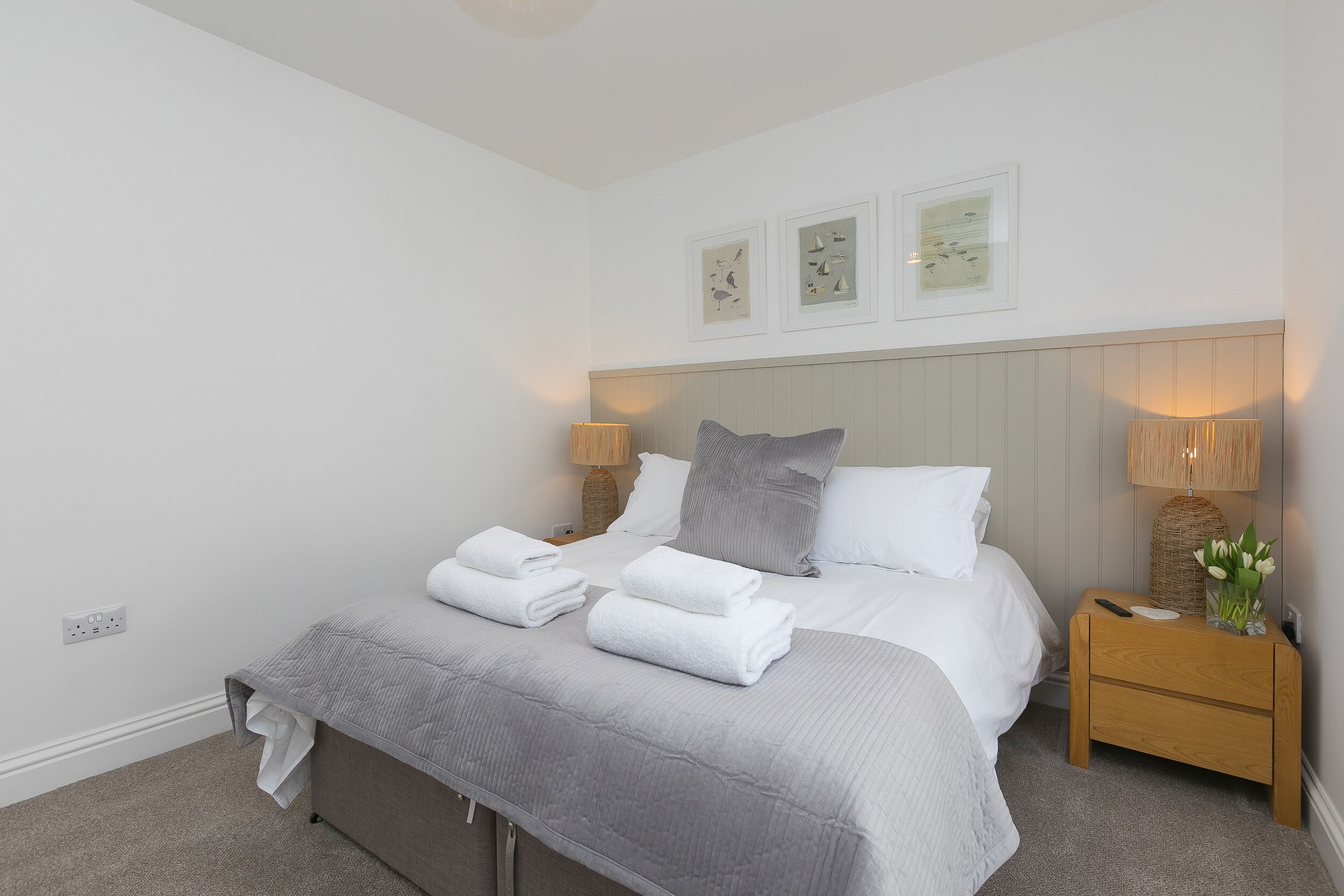 A neatly made bed with white linens and a grey blanket, two bedside tables with lamps, and wall art above the bed.
