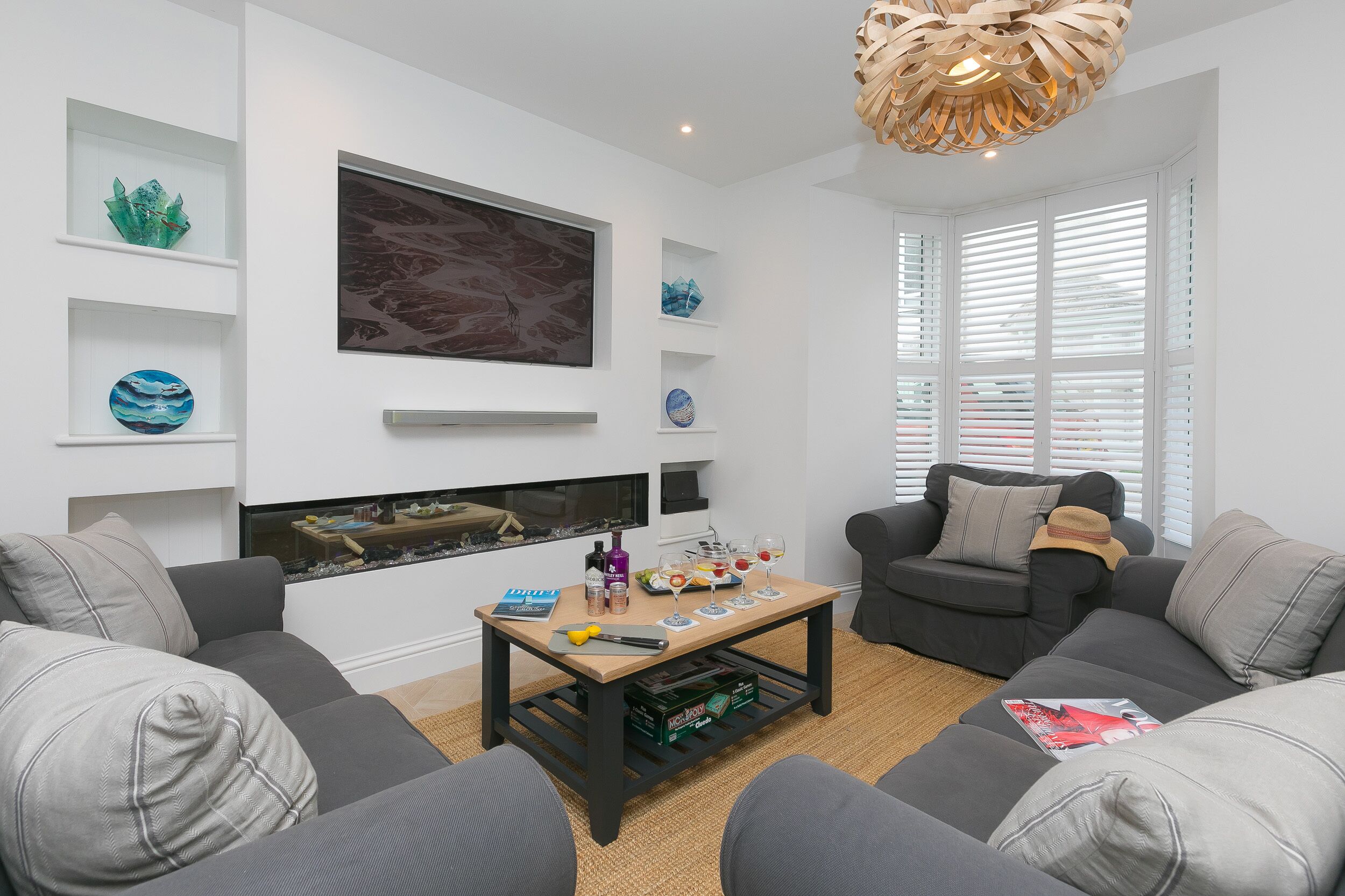 A modern living room with grey sofas, a wooden coffee table, and decorative glass pieces on shelves.