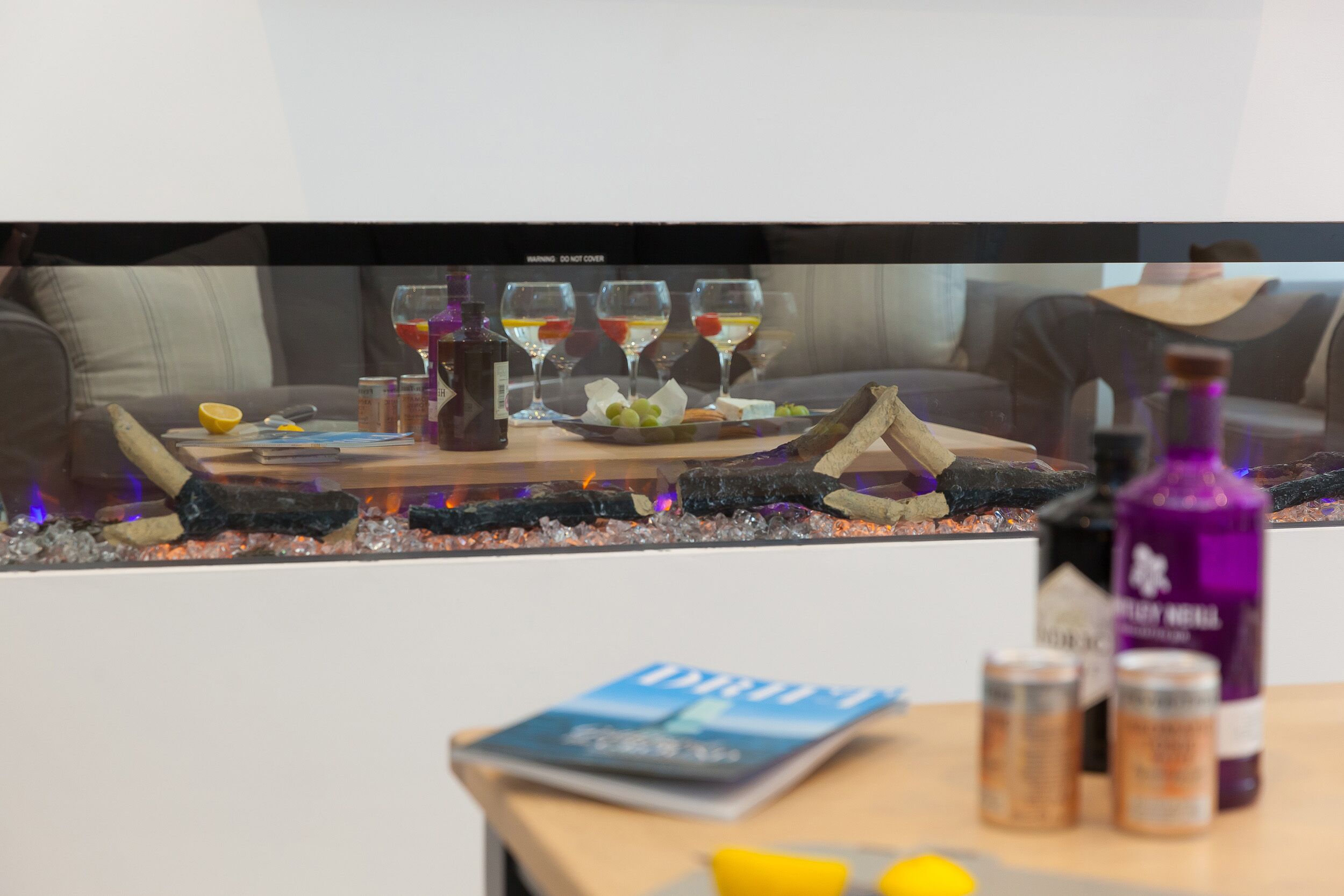 A room with a television displaying a scene of a dining table with glasses and a bottle. There are also some containers and a book on a table in the foreground.