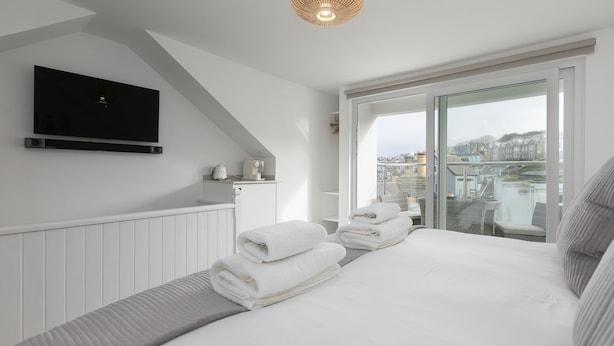 A modern hotel room with a bed, a flat-screen TV mounted on the wall, and a balcony with a view of the city. - Pebbles (St Ives)