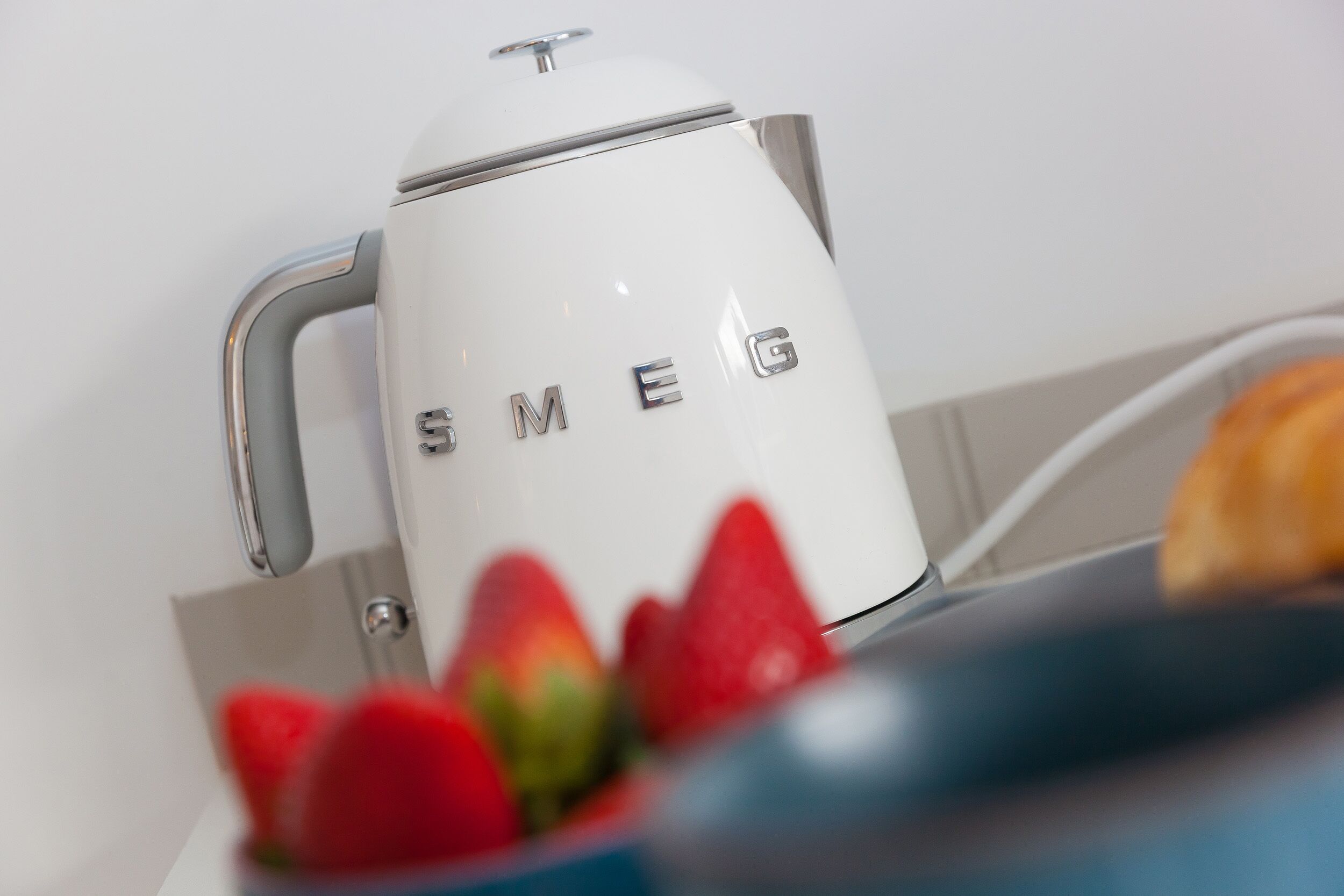 Uma cafeteira branca com a marca "SMEG" em uma parede branca.