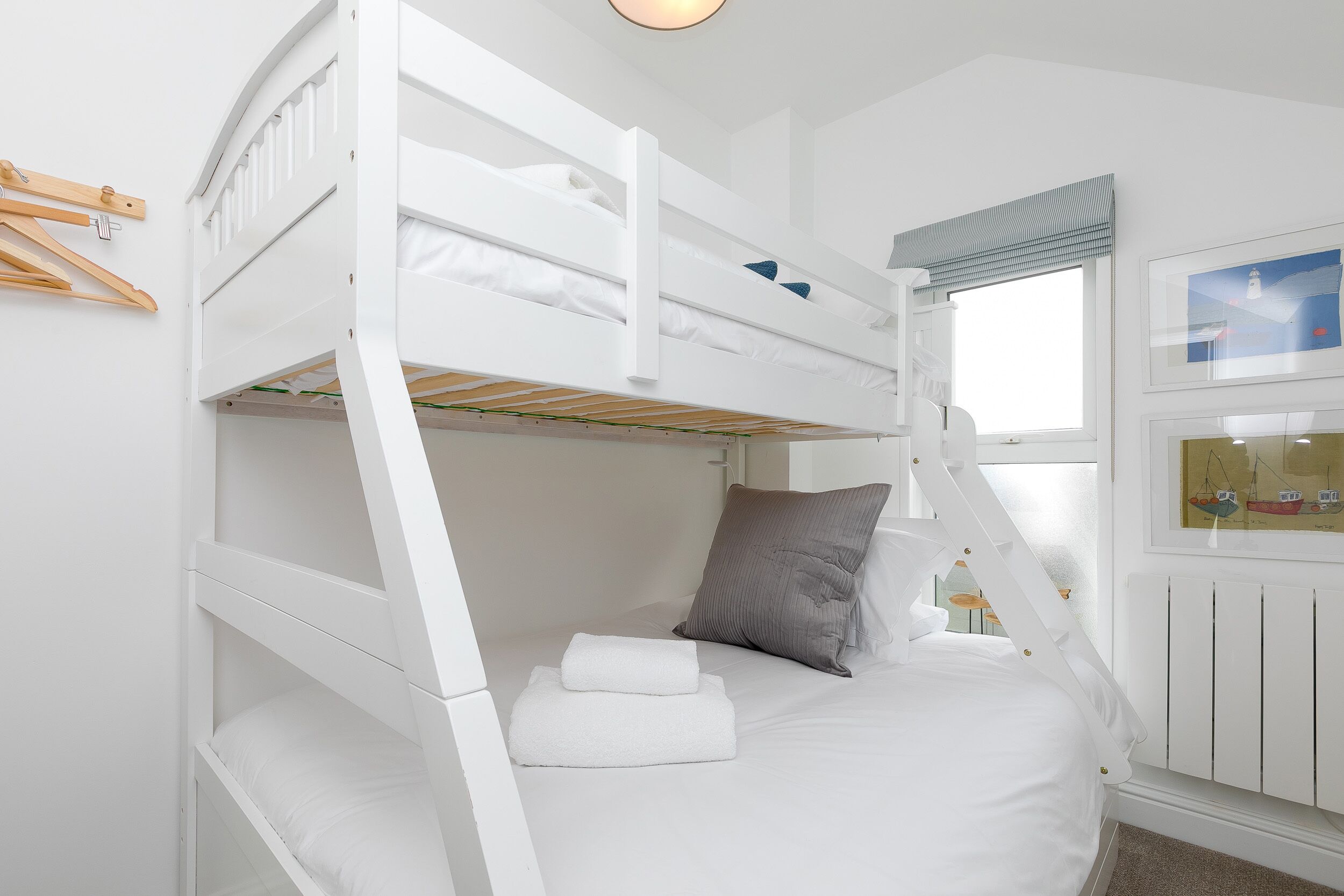 Habitación con literas, ropa de cama blanca, una escalera y una ventana con vistas a barcos.