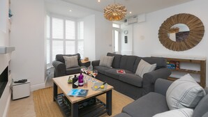 A modern living room with a sofa set, a coffee table with drinks and snacks, and a unique wooden mirror on the wall. - Pebbles (St Ives)