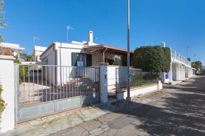 Um edifício residencial com portão fechado, varanda coberta e escadaria até a entrada.