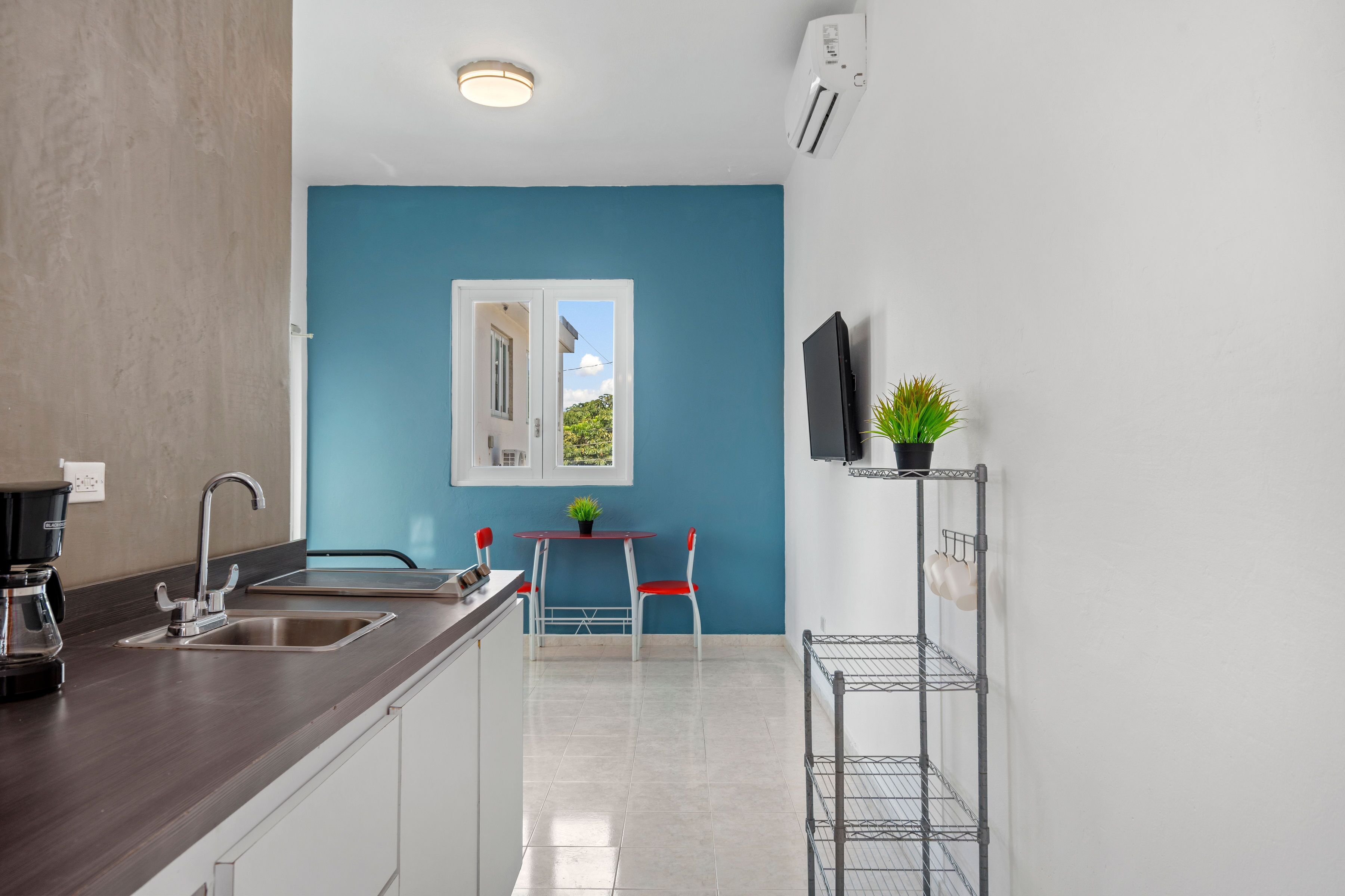 A modern kitchen with a blue accent wall, a dining area with a small table and chairs, and a TV mounted on the wall.