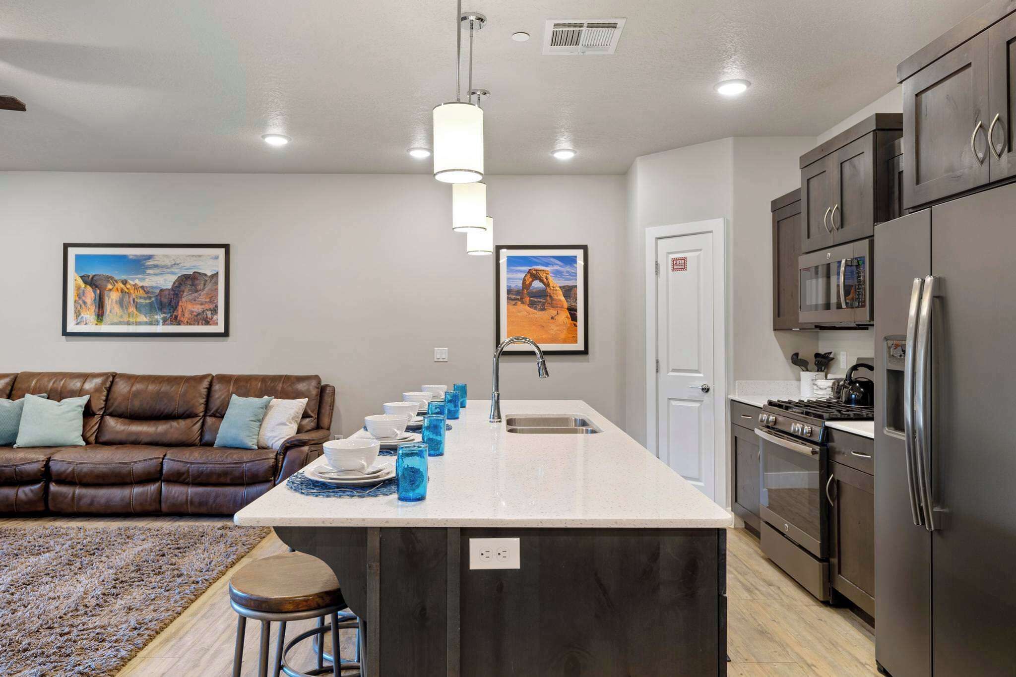 A modern kitchen with a central island, stainless steel appliances, and a seating area with a brown leather couch.