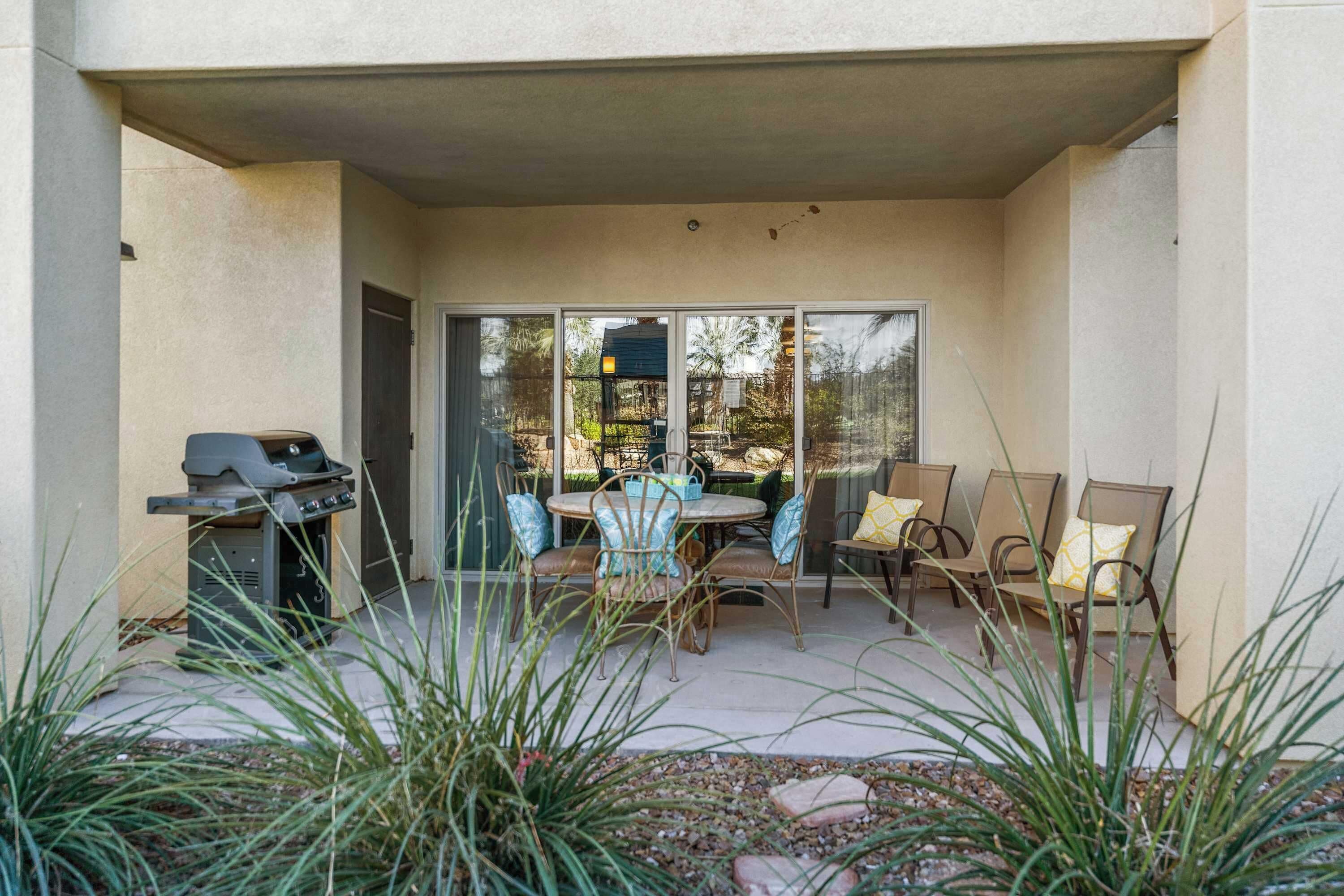 An outdoor patio with a grill, a table with chairs, and a view through a glass door.