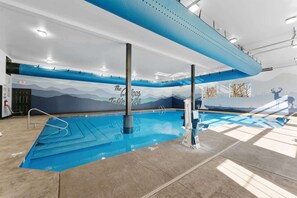 Una piscina interior con un mural de montañas, zona de piscina despejada y señal de salida visible.