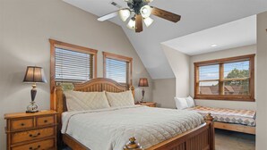 A bedroom with a large bed, two bedside tables, a ceiling fan, and a window with blinds. - Kemper's Cabin by Silver Dollar City - Ideally Located (Branson)