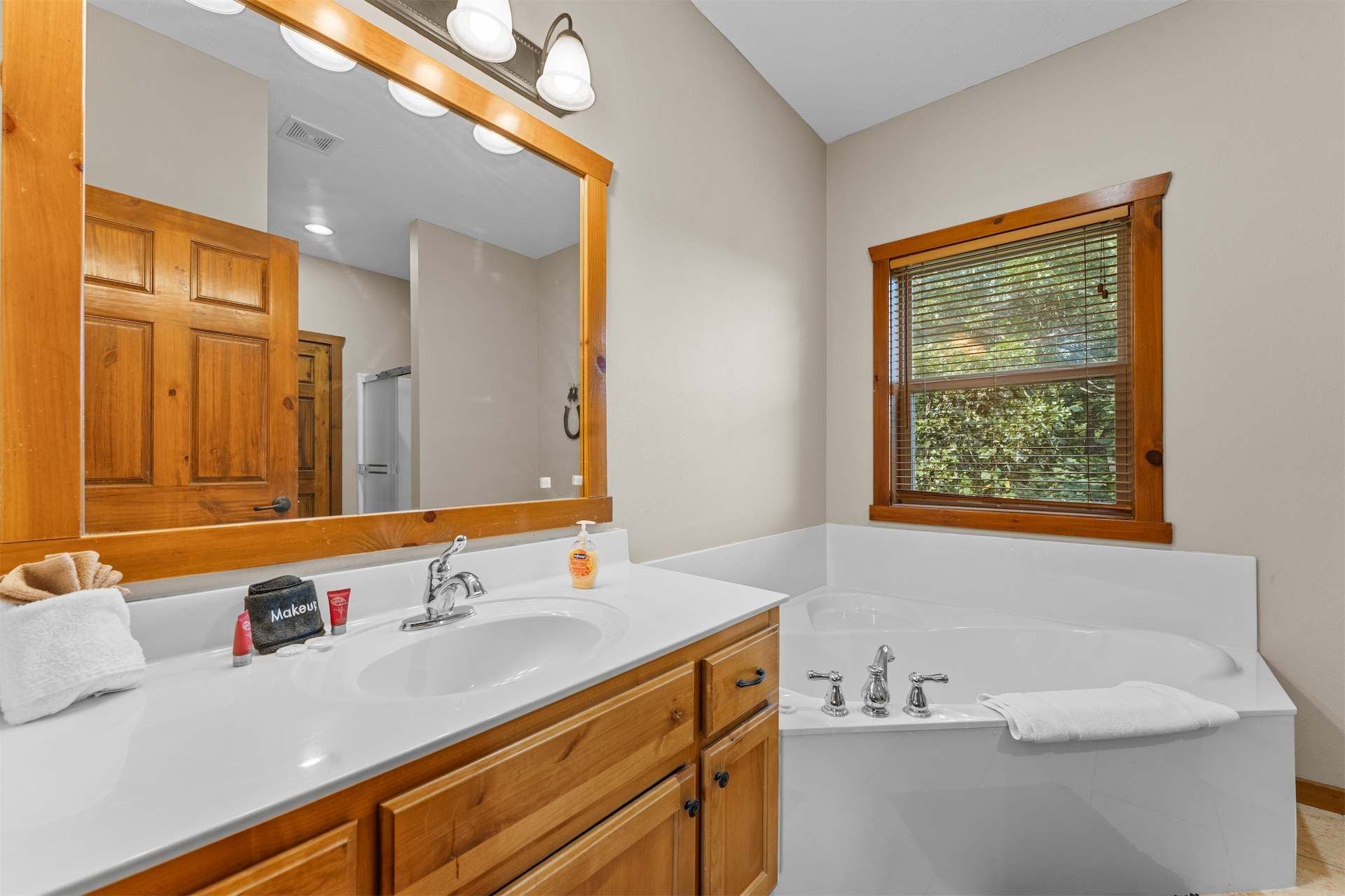 Une salle de bain avec deux lavabos, un grand miroir, des meubles en bois et une fenêtre avec des stores.