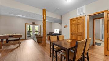 A spacious living room with a wooden dining table, comfortable seating, and a television.