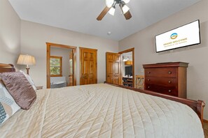 Une chambre à coucher comprenant un lit, une commode en bois, un ventilateur de plafond et un téléviseur fixé au mur qui affiche un message de bienvenue.