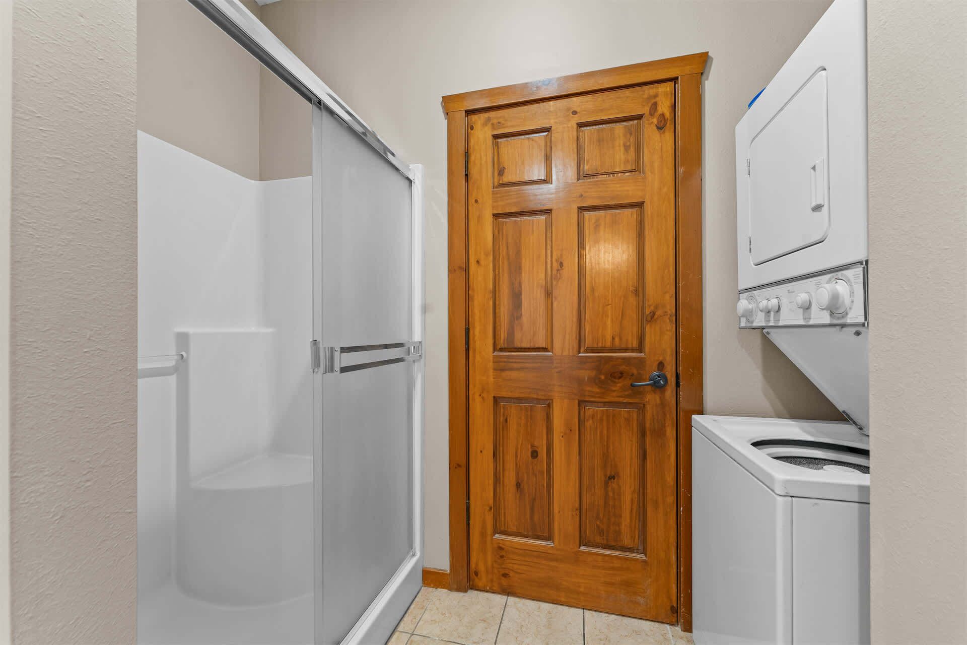 A bathroom with a wooden door, a shower enclosure, and a washing machine.