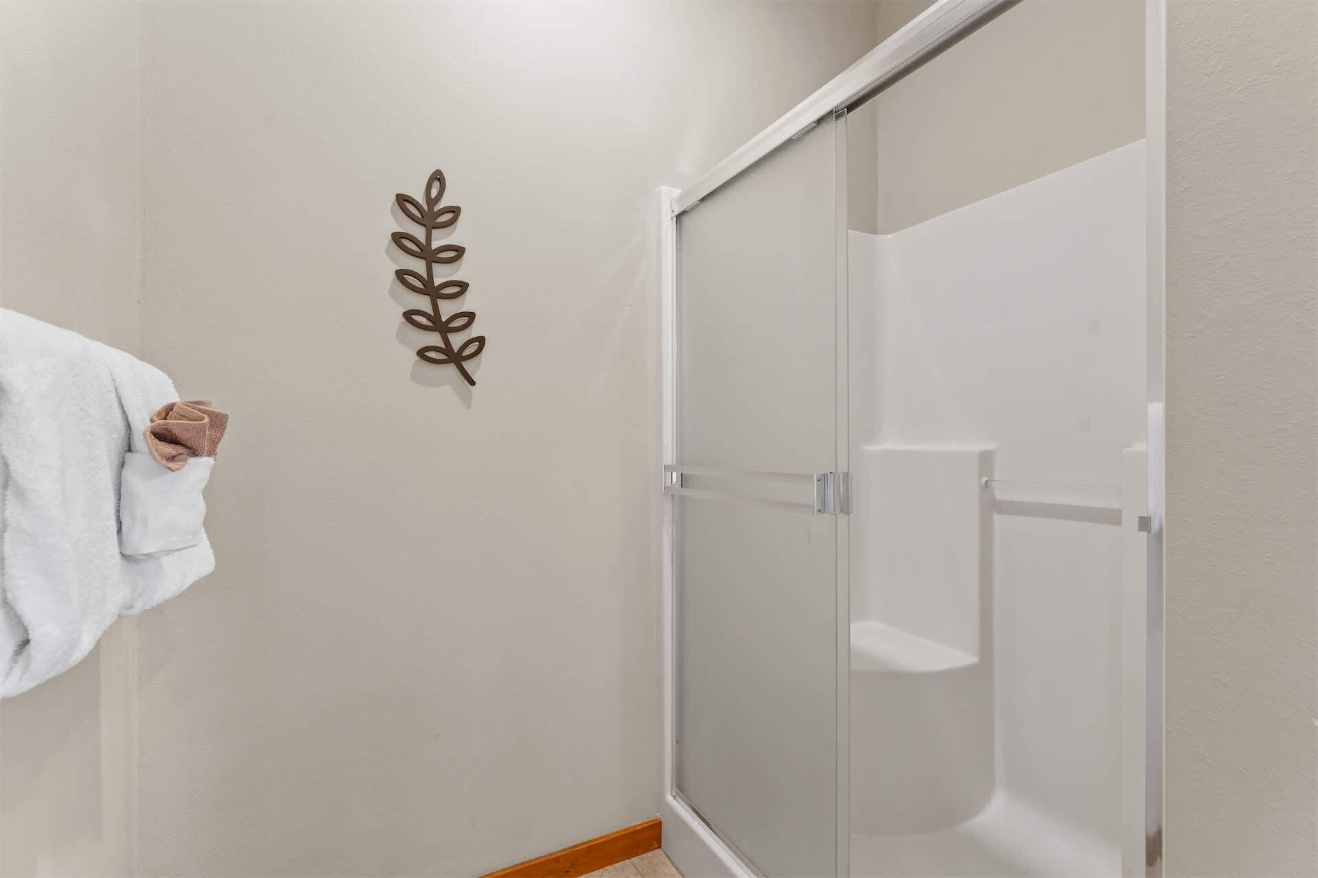 Une salle de bain avec une serviette blanche accrochée au mur, une douche en verre et une feuille décorative fixée au mur.