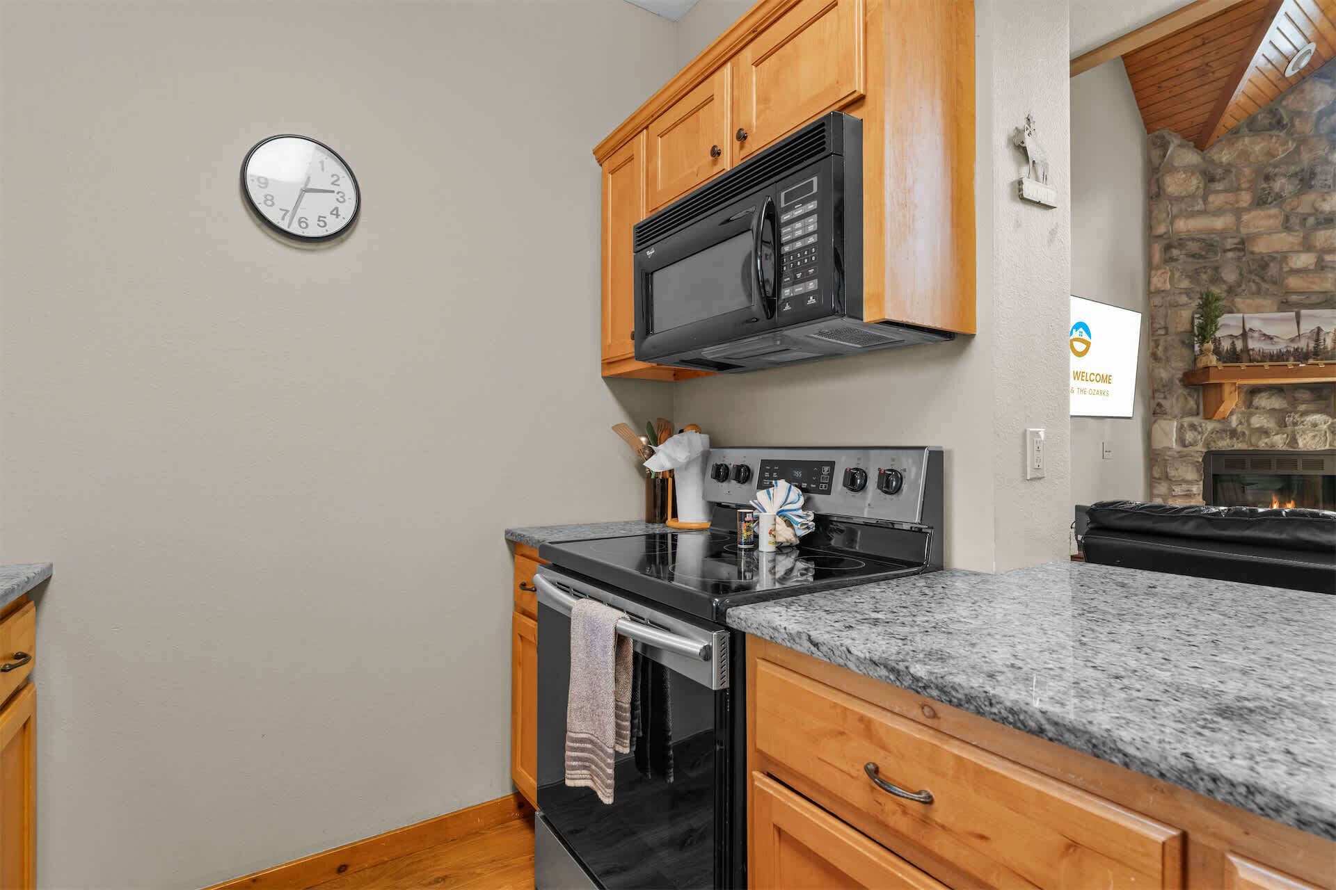 Una cocina con armarios de madera, un microondas negro, una estufa y un reloj en la pared.