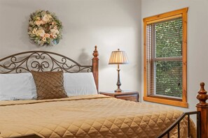 Un dormitorio con cama, lámpara de noche, ventana con persianas y un adorno decorativo en la pared.