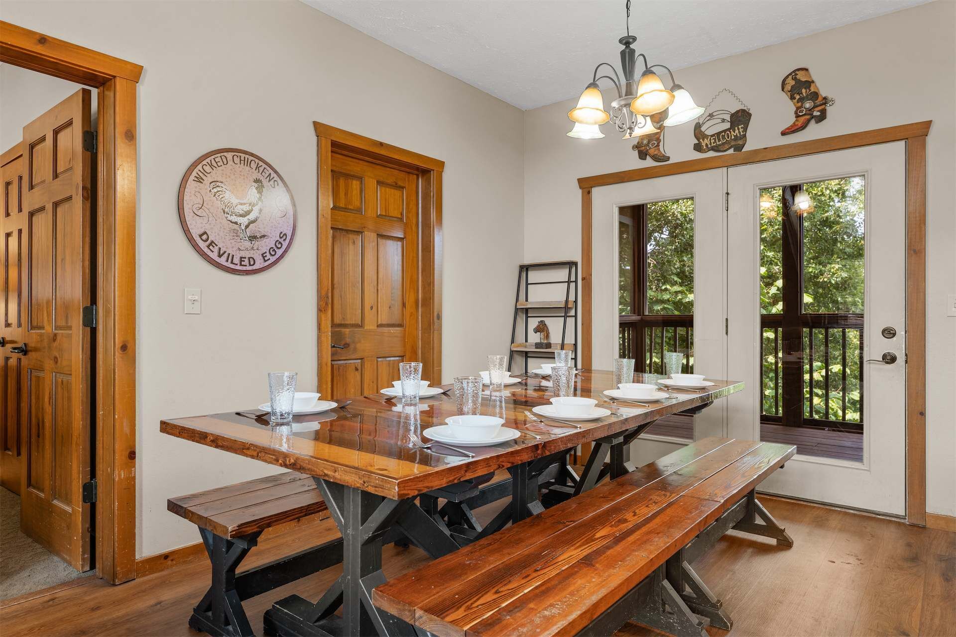 A dining area with a long wooden table set for six, benches, and a chandelier.