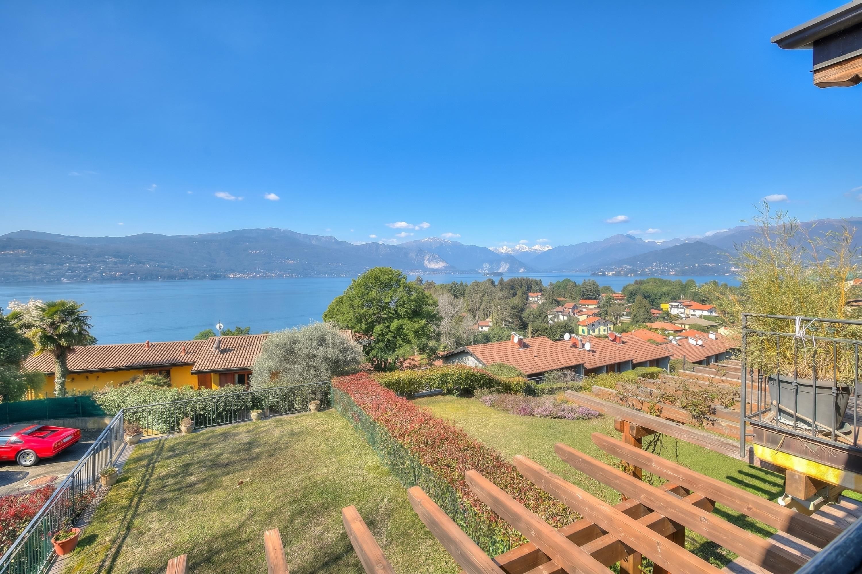 A residential area with a view of a lake and mountains, wooden deck, and a red sports car.