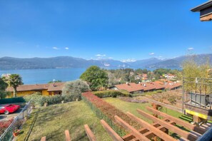 A residential area with a view of a lake and mountains, wooden deck, and a red sports car. - La Brezza Del Lago Maggiore: Apartment With Terrace and View (Laveno Mombello)
