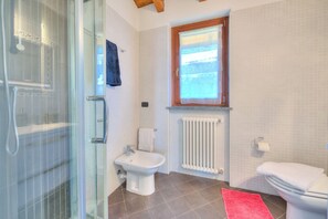 A bathroom with a glass shower enclosure, a bidet, a toilet, and a window with a wooden frame. - La Brezza Del Lago Maggiore: Apartment With Terrace and View (Laveno Mombello)