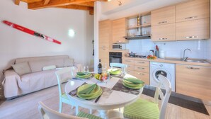 A modern kitchen with wooden cabinets, a dining area with a round table and chairs, and a sofa in the living area. - La Brezza Del Lago Maggiore: Apartment With Terrace and View (Laveno Mombello)