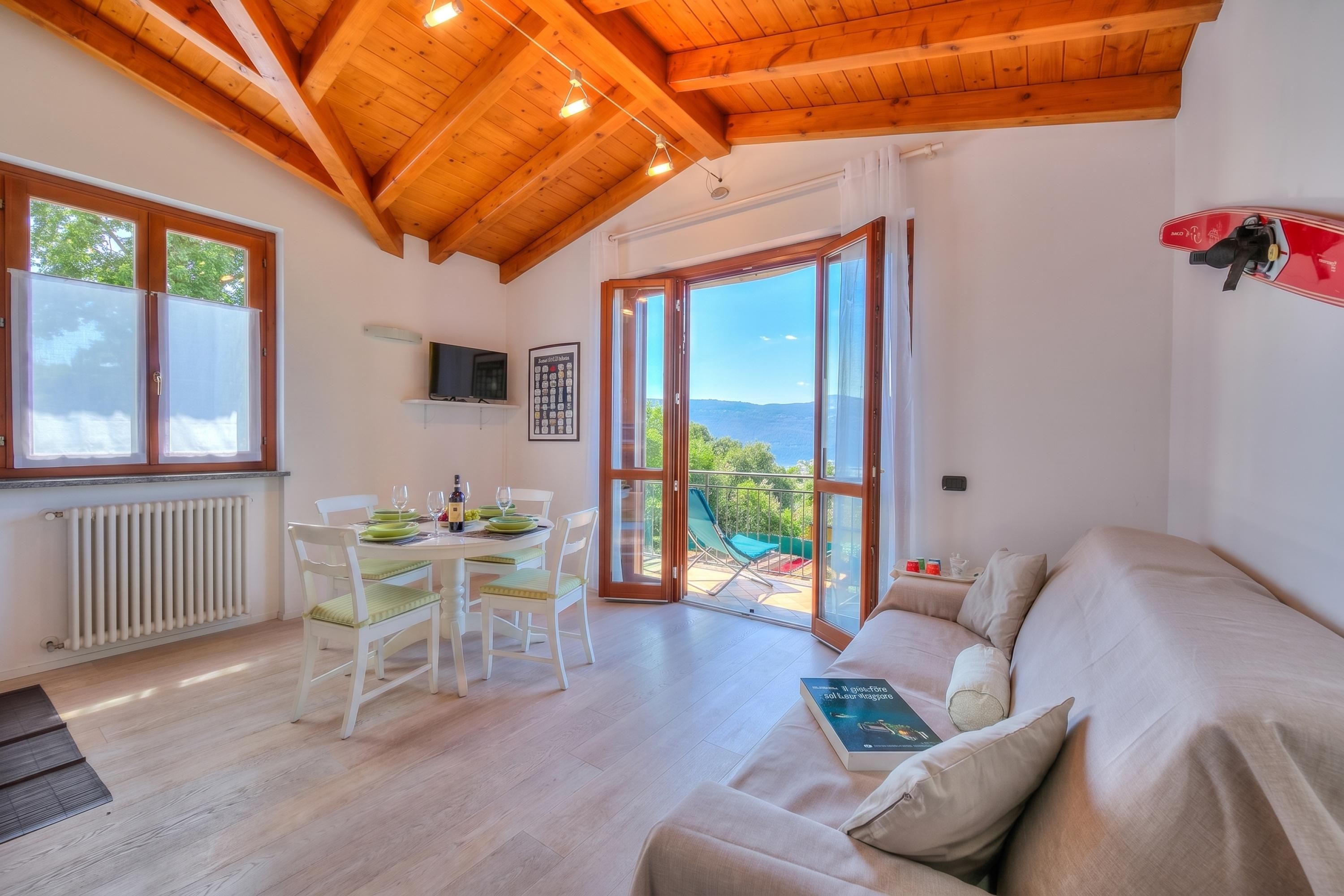 A room with a wooden ceiling, a dining table with chairs, a sofa, and a large window with a view.