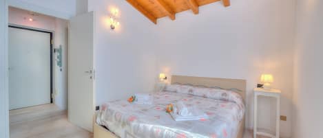 A bedroom with a wooden ceiling, a bed with floral bedding, bedside lamps, and a white nightstand.