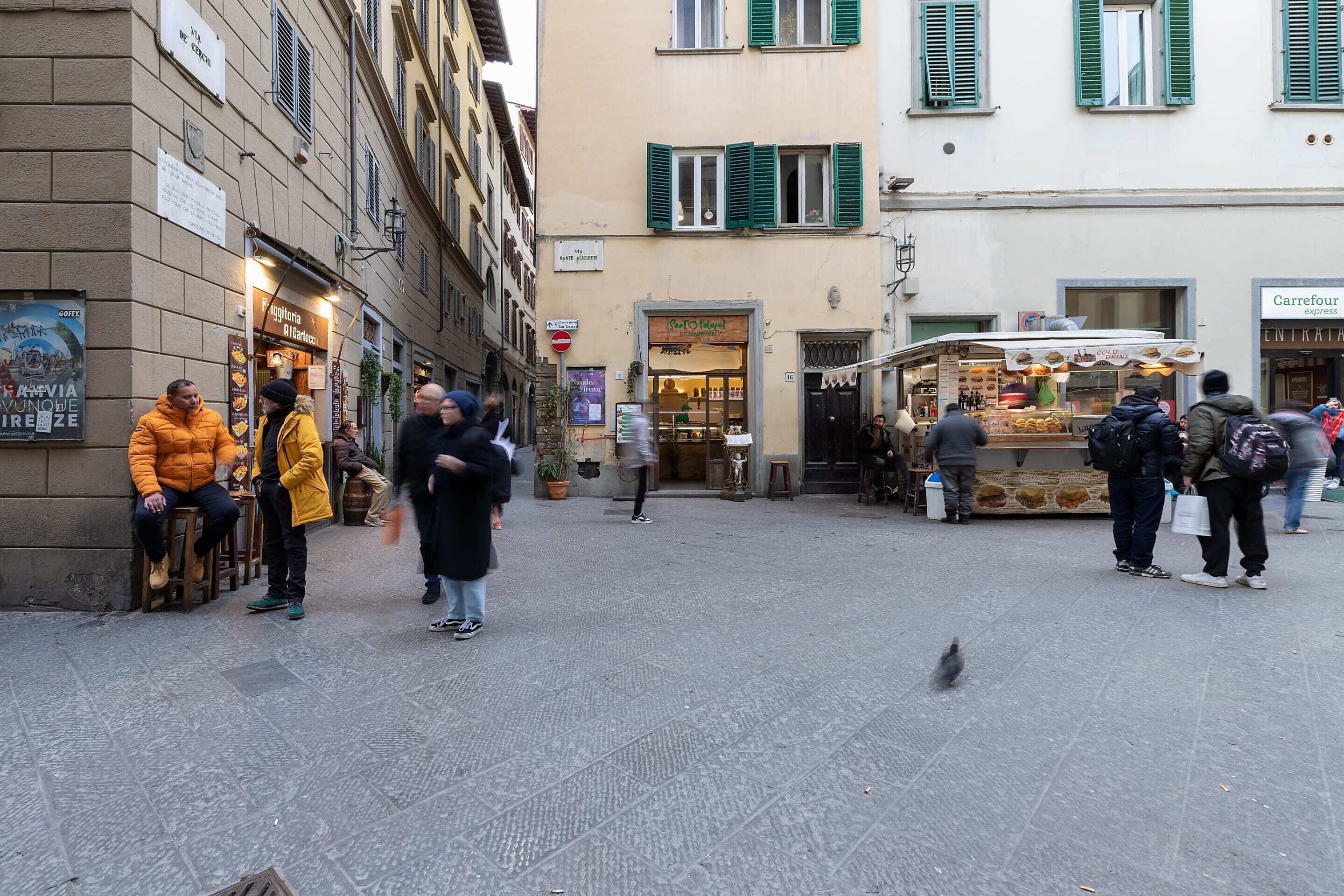 Et gadesceneri med folk, der sidder og står i nærheden af caféer og butikker.