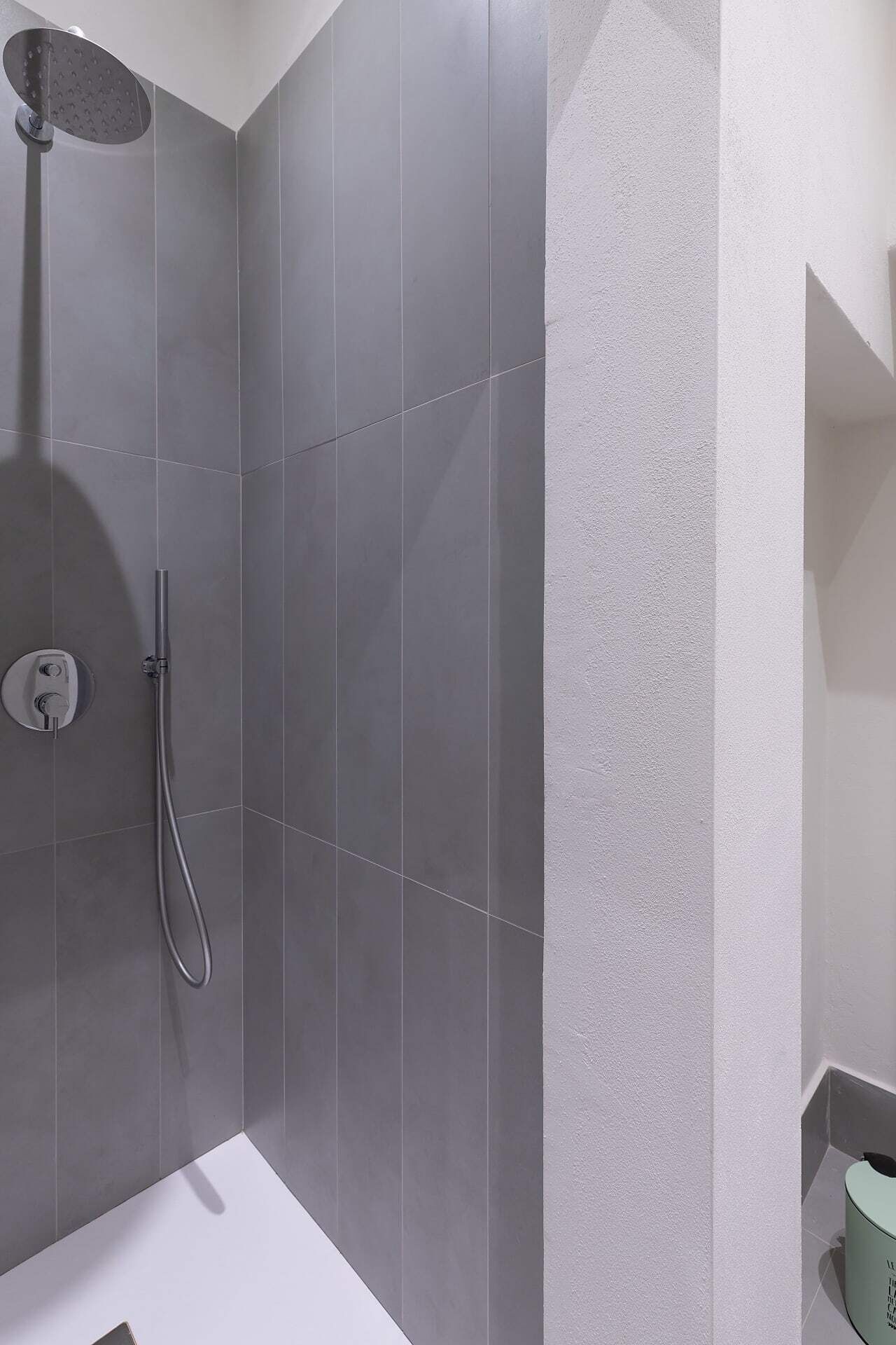 Ein modernes Badezimmer mit grauen Fliesen, einer Dusche inklusive Handbrause und einer weißen Badewanne.