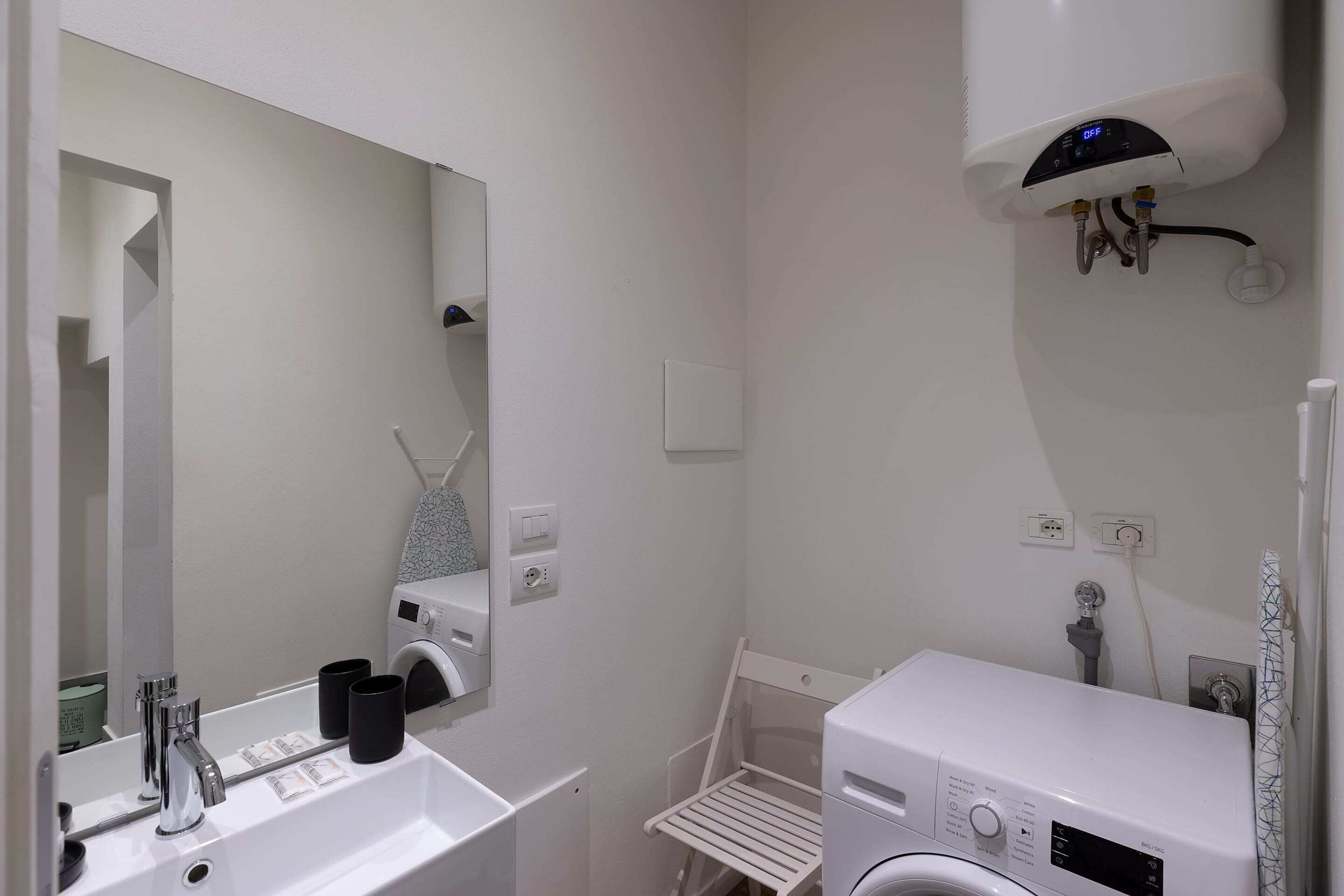 A modern bathroom with a sink, mirror, and a washing machine.