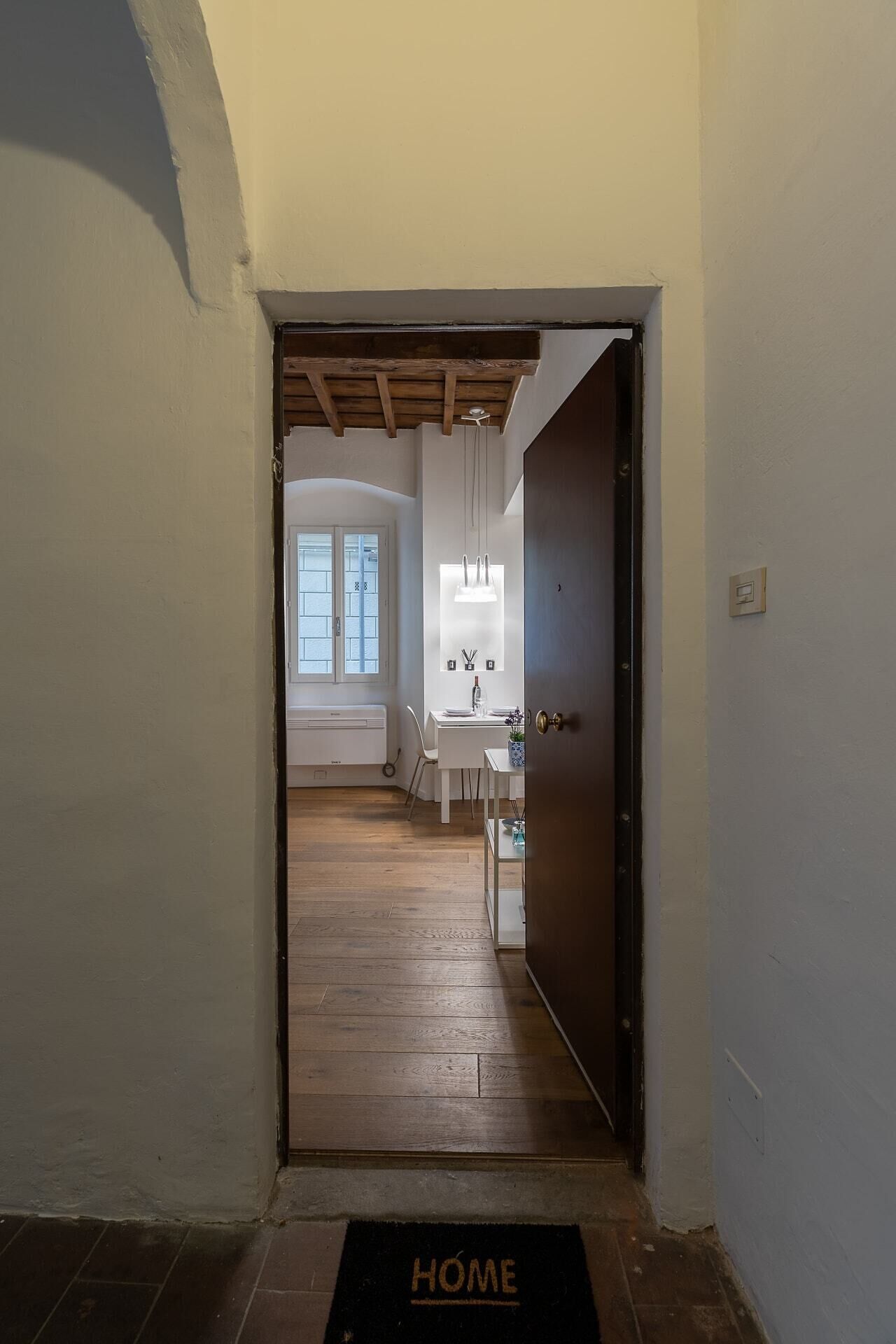 A hallway leading to a kitchen with a wooden ceiling, a white radiator, and a door with a 'HOME' mat.