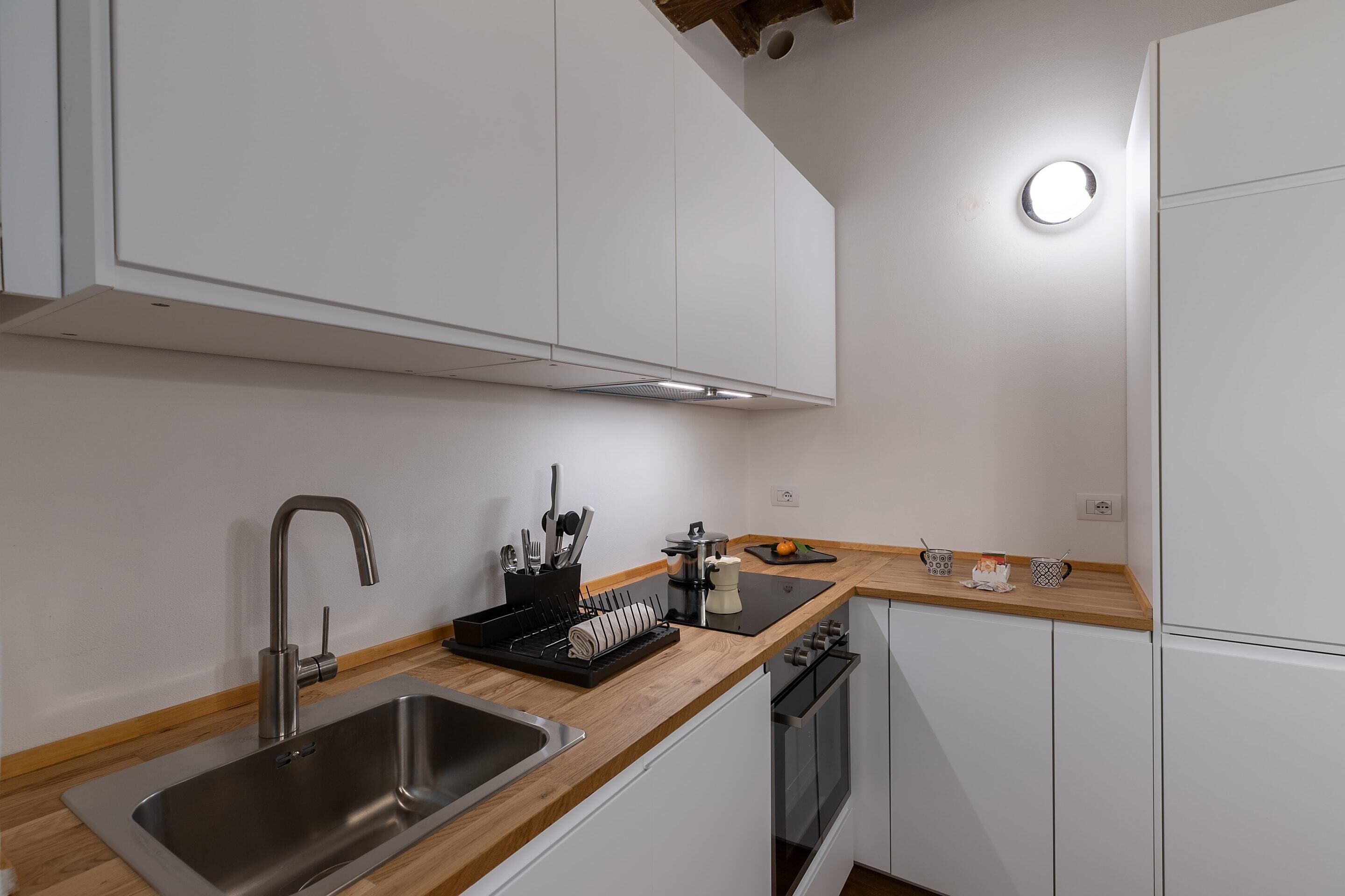 Een moderne keuken met witte kastjes, een roestvrijstalen spoelbak, een houten werkblad en een inbouw vaatwasser.