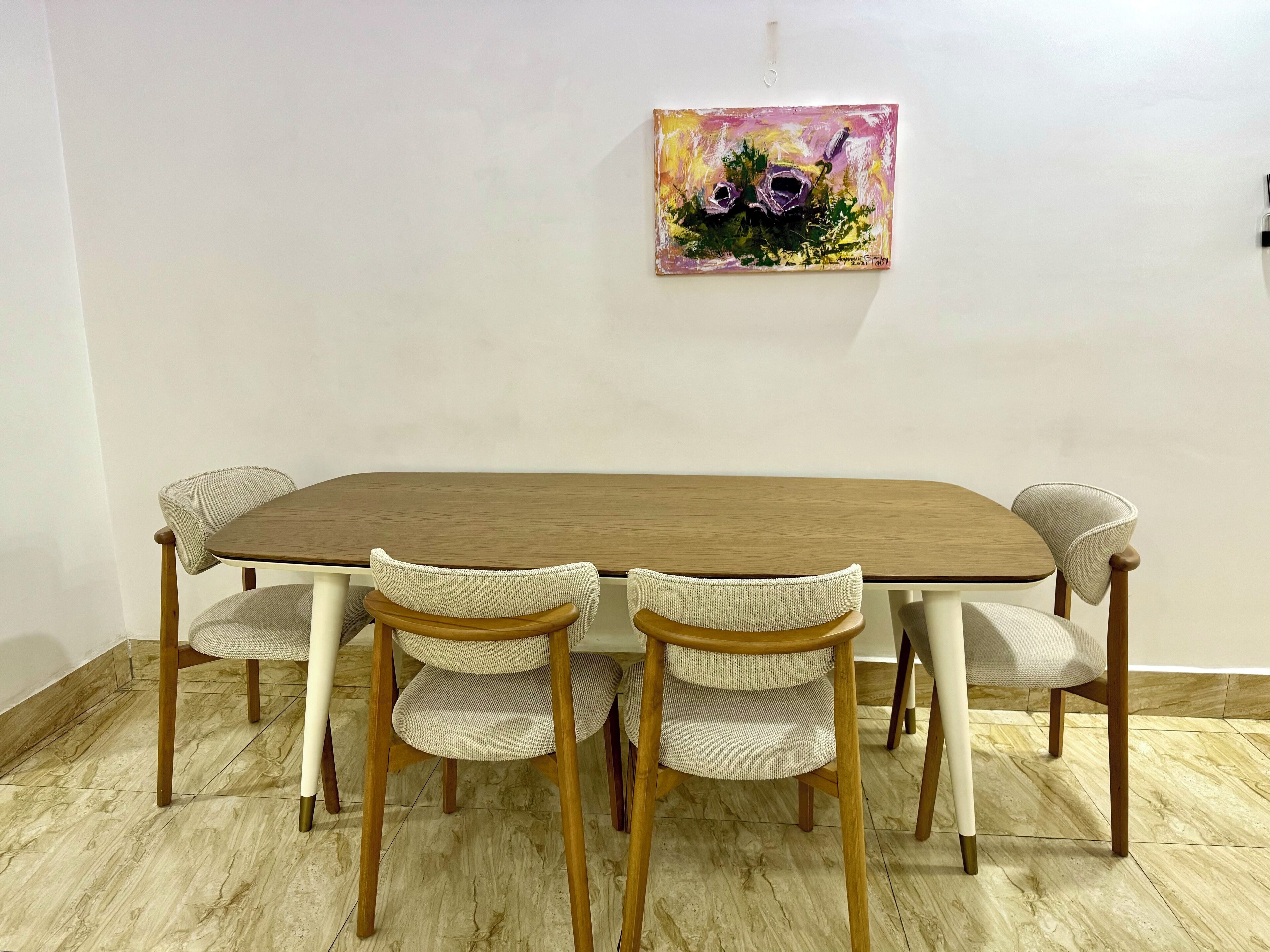 A dining table with four chairs, a painting on the wall, and a tiled floor.