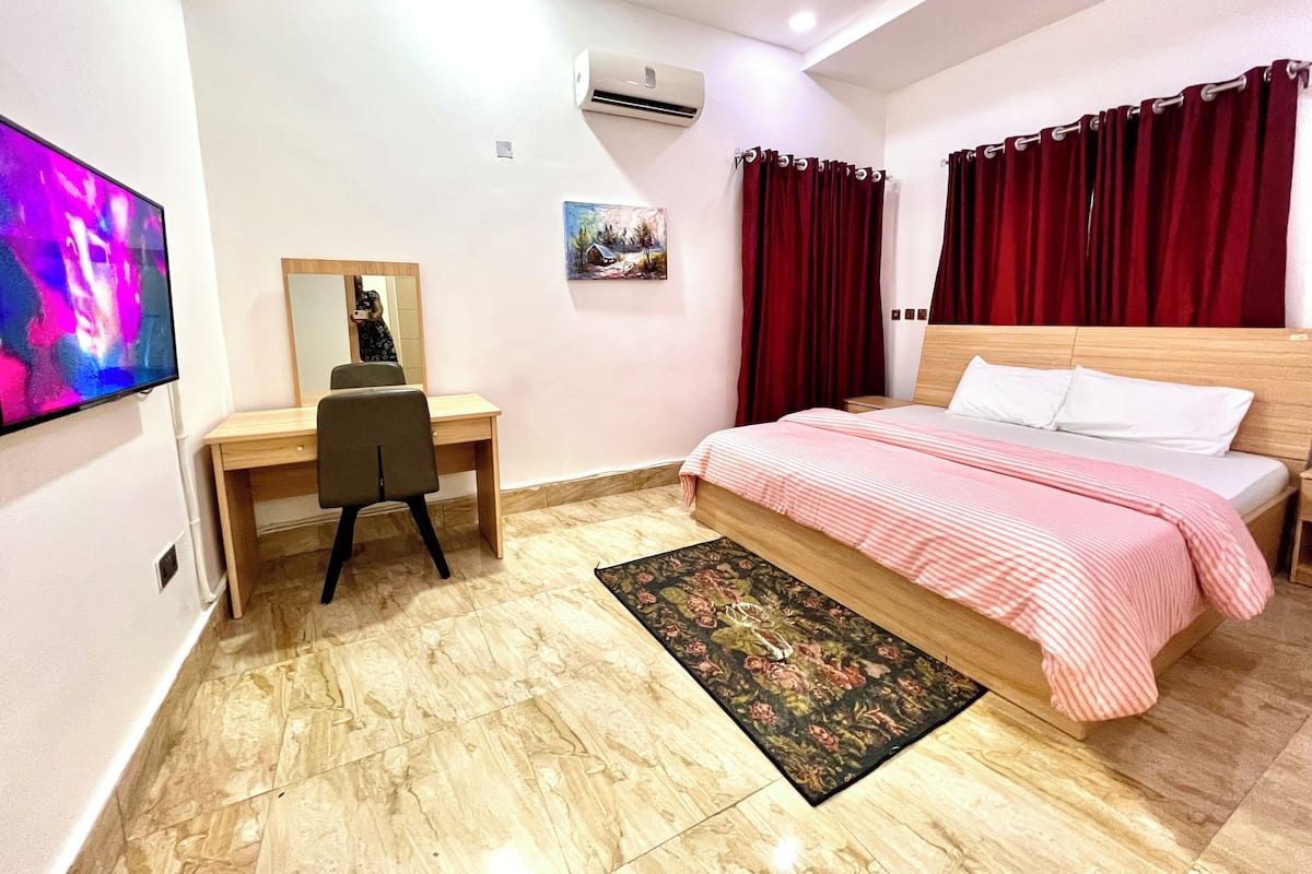 Une chambre avec un lit, un bureau, une chaise, un climatiseur et un téléviseur.